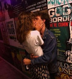 a man and woman kissing each other in front of a wall with posters on it