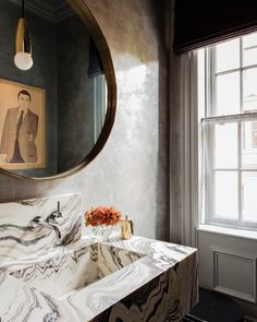 a bathroom with marble counter tops and a round mirror over the sink in front of a window