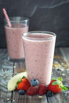 a smoothie with strawberries, bananas and blueberries on the side next to it