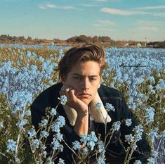 a young man sitting in a field of blue flowers with his hands on his face