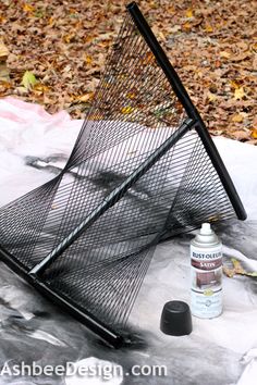 a wire basket sitting on top of a table covered in leaves and paint next to a bottle