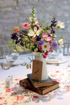 a vase filled with lots of flowers on top of a wooden table next to a stack of books