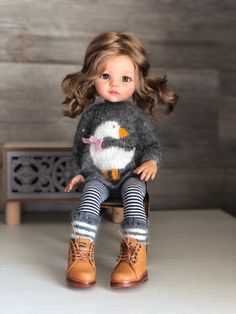a doll sitting on top of a wooden table next to a bench with a penguin sweater and leggings