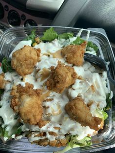 a plastic container filled with salad covered in chicken nuggies and ranch dressing on top of lettuce