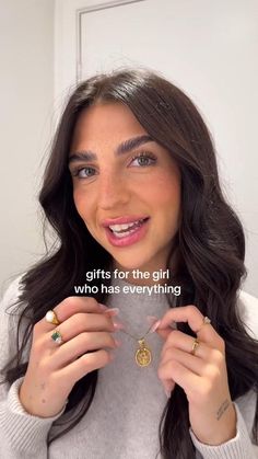 a woman with long dark hair holding two gold rings in front of her face and the words gifts for the girl who has everything written on it