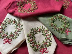 four embroidered napkins with bows and wreath designs on them, all in different colors