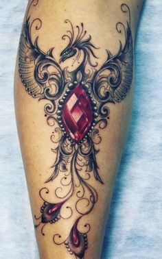 a woman's leg with an intricate tattoo design and a red jewel on it