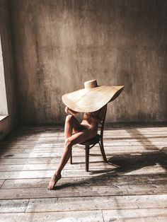 a nude woman sitting in a chair with a straw hat on her head and legs