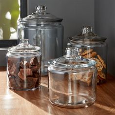 three glass canisters filled with cookies on top of a wooden table