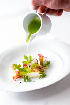 a person pouring sauce on a plate with vegetables