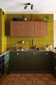 a kitchen with wooden cabinets and green tile backsplash, wood flooring and counter tops