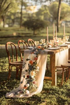 a long table with flowers and candles on it in the middle of a grassy field