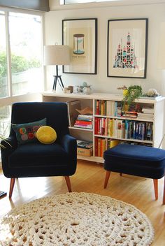 a living room with two chairs and a rug in front of the window, next to a bookshelf