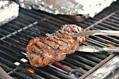 a steak is cooking on the grill with tongs