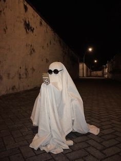 a ghost with sunglasses and a cell phone in his hands is sitting on the ground