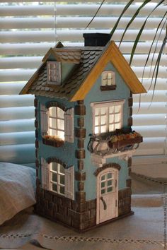 a blue doll house sitting on top of a bed next to a window covered in blinds