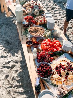 a long table filled with lots of food on top of a sandy beach next to the ocean