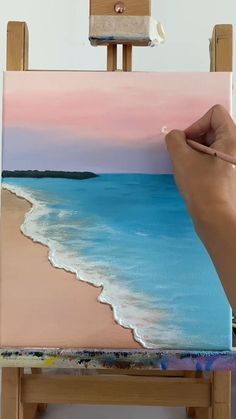a person is painting on an easel with a pink and blue sky in the background