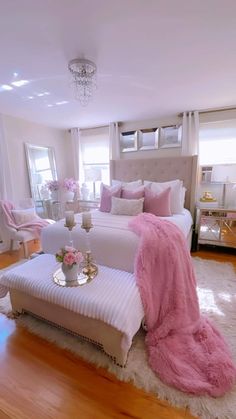 a white bed with pink pillows and blankets on it in a room filled with furniture