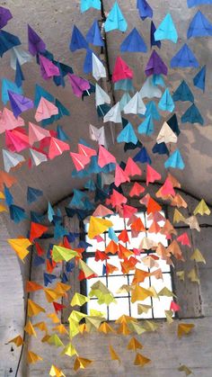 colorful origami birds hanging from the ceiling in an old building with a stained glass window