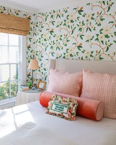 a bedroom with floral wallpaper and pink bedding, along with an orange pillow