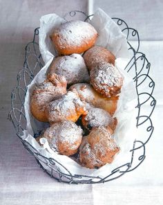 powdered doughnuts in a wire basket on a white tablecloth covered table