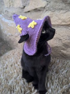 a black cat wearing a purple knitted hat with yellow flowers on it's ears