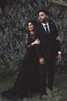a man and woman standing next to each other in front of some bushes wearing formal clothes
