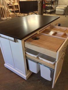a kitchen island with two trash cans under it and an open drawer in the middle