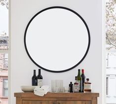 a round mirror on the wall above a wooden cabinet with bottles and glasses sitting on it