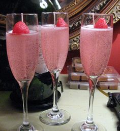 two champagne flutes filled with pink liquid and topped with raspberries on a table