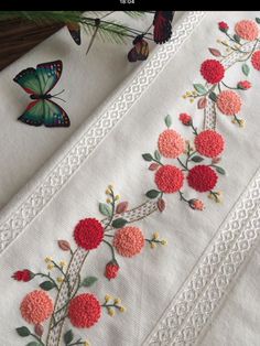 embroidered flowers and butterflies on white linens next to pine tree branch with butterfly in background