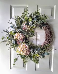 a wreath is hanging on the front door with flowers and greenery around it,