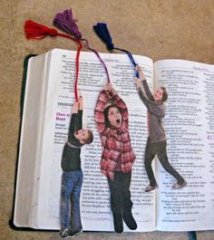 an open book with pictures of people hanging from it's sides and two children standing on the pages