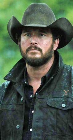 a man with a beard wearing a black shirt and cowboy hat looking at the camera