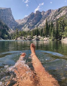 a person laying on their back in the water with mountains in the background and trees around them