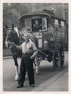 an old black and white photo of two people standing next to a horse drawn carriage