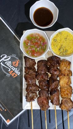 a plate with skewers of meat and dipping sauces