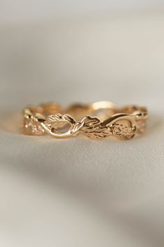 a gold wedding band with leaves on the side, sitting on top of a white surface