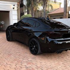 a black sports car is parked in front of a house with palm trees on the driveway