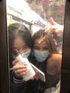 two women wearing face masks and holding up their hands to take a selfie in the mirror