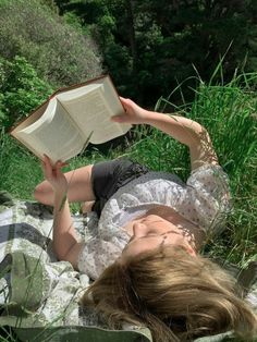 a woman is laying down reading a book in the grass with her eyes closed and head resting on an open book