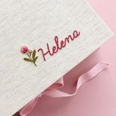 embroidered name on fabric with pink ribbon and flower in center, laying on light pink surface