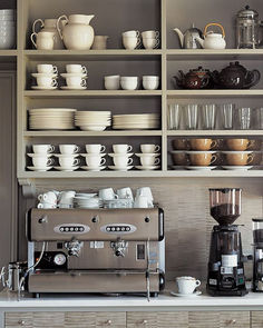 a coffee machine sitting on top of a counter next to shelves filled with cups and saucers