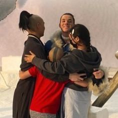 three people hugging each other in front of a snow - covered area with an animal statue behind them