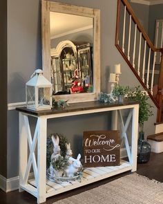 a white console table with a welcome sign on top and some decorations around it in front of a staircase