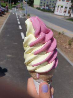 a hand holding an ice cream cone with pink and white icing