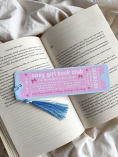 an open book with a tassel on top of it next to a pink and blue bookmark