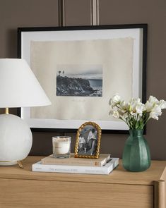a table with a lamp, vase and pictures on it next to a framed photograph
