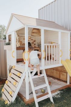 a toddler climbing up the side of a white wooden house with a yellow slide